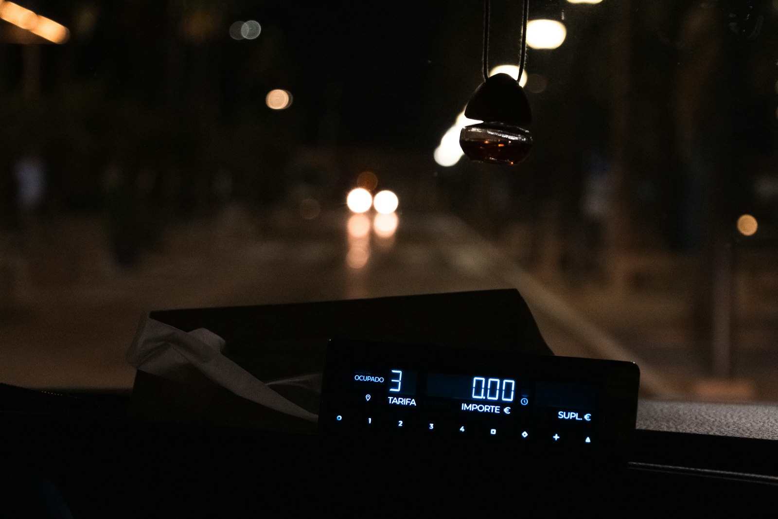 A taxi fare meter on a dashboard at night showing 0.00, with blurred street lights through the windscreen