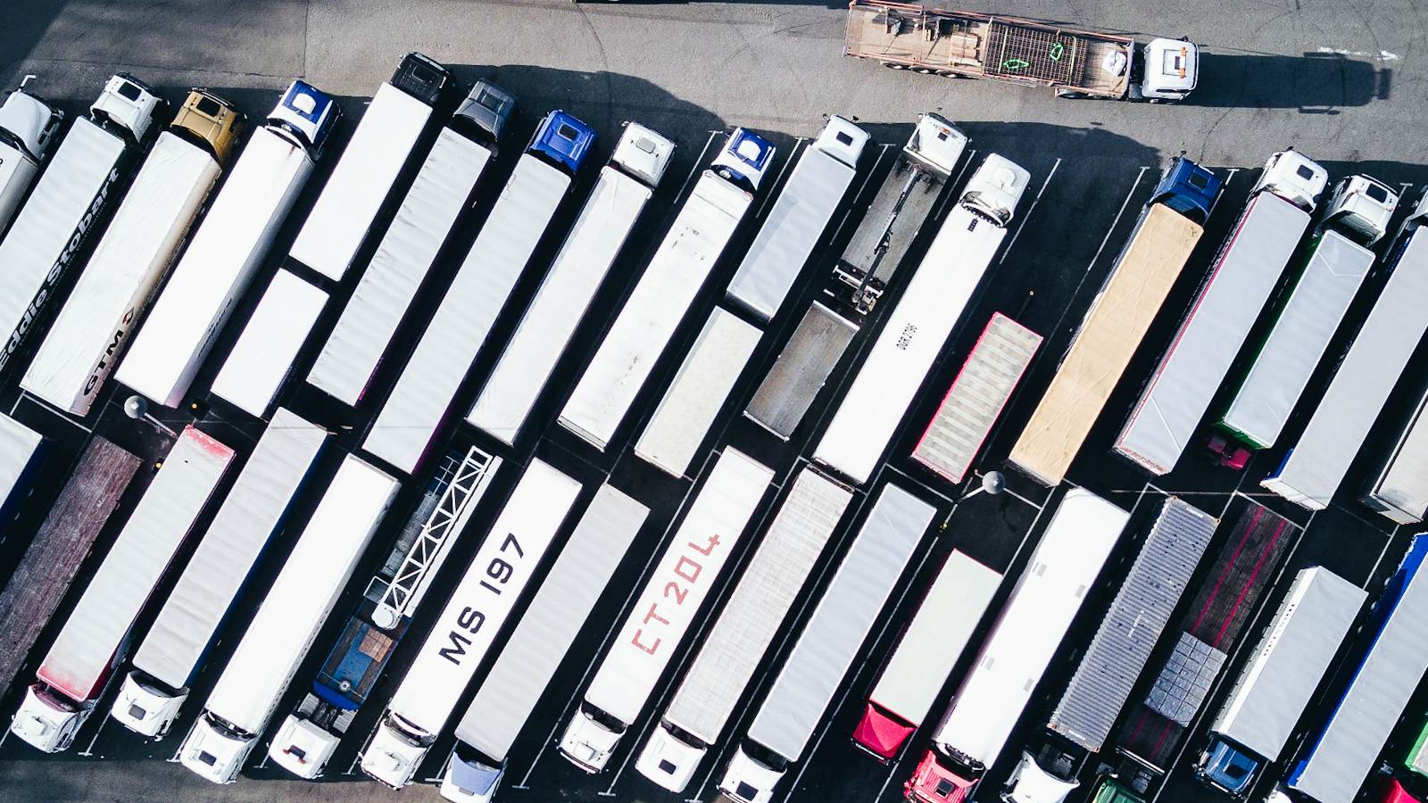 Aerial view of a truck park with rows of articulated lorries and trailers parked at an angle, seen from directly above