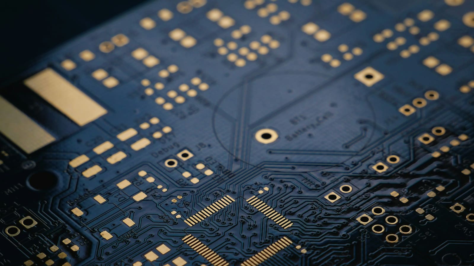 Close-up of a dark blue circuit board with gold pads and fine traces