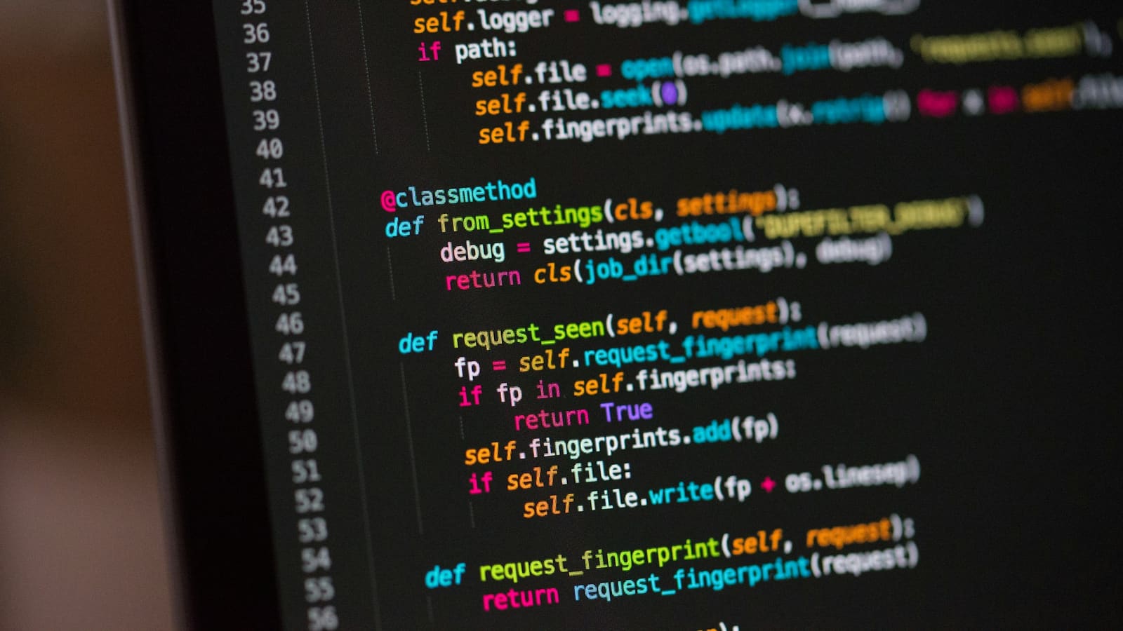 Colourful Python code with line numbers on a dark monitor, tilted view