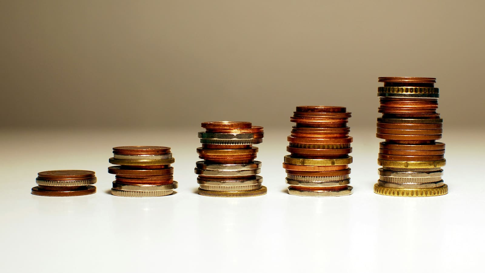Five stacks of coins growing taller from left to right on a pale surface
