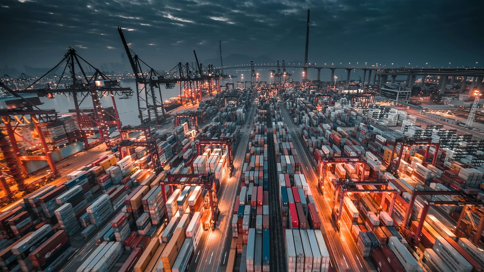 Wide aerial view of a container port at dusk with cranes and stacked containers