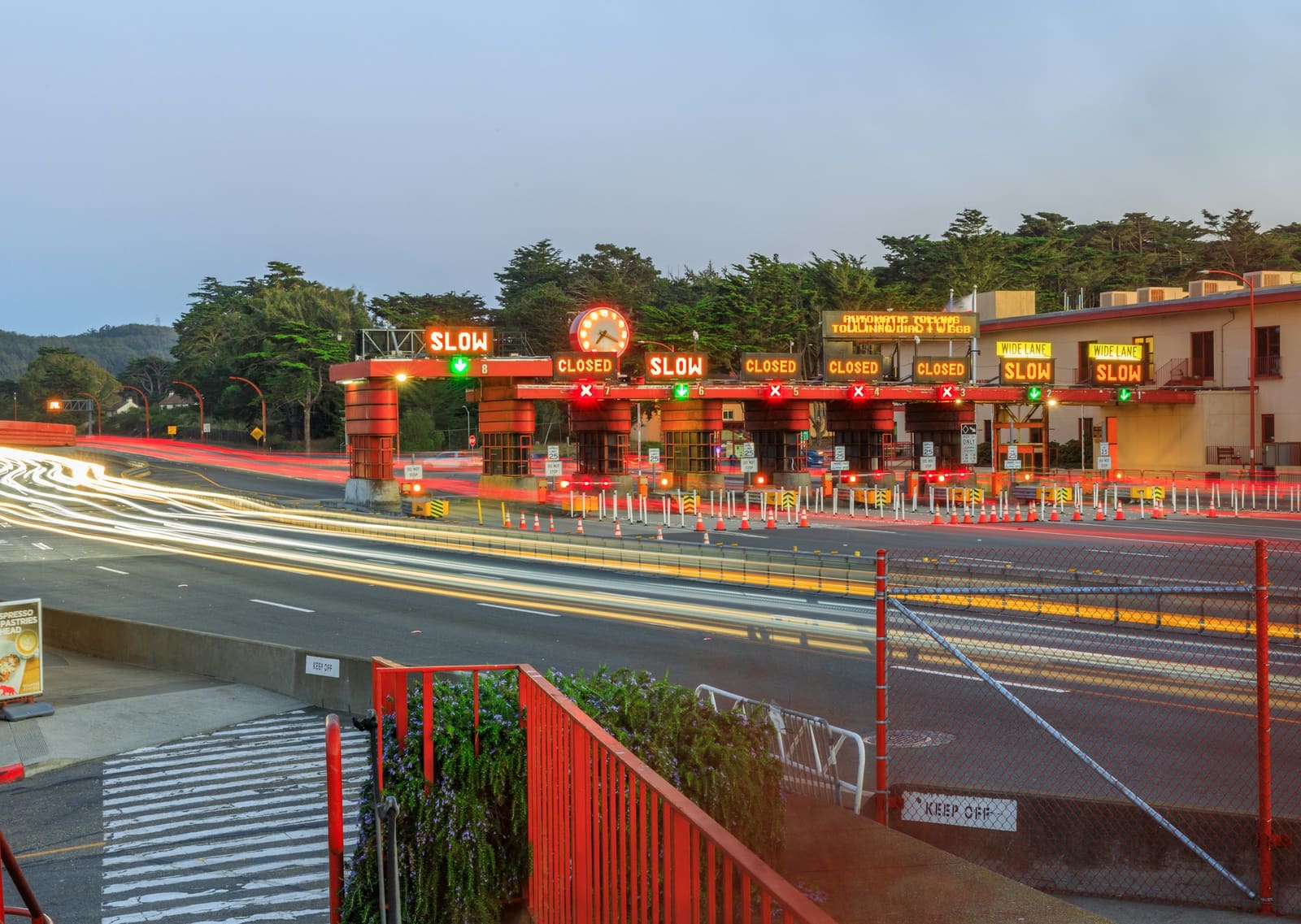 The Golden Gate Bridge toll plaza at dusk, with lit lane signs reading slow and closed above the booths and light trails from passing traffic