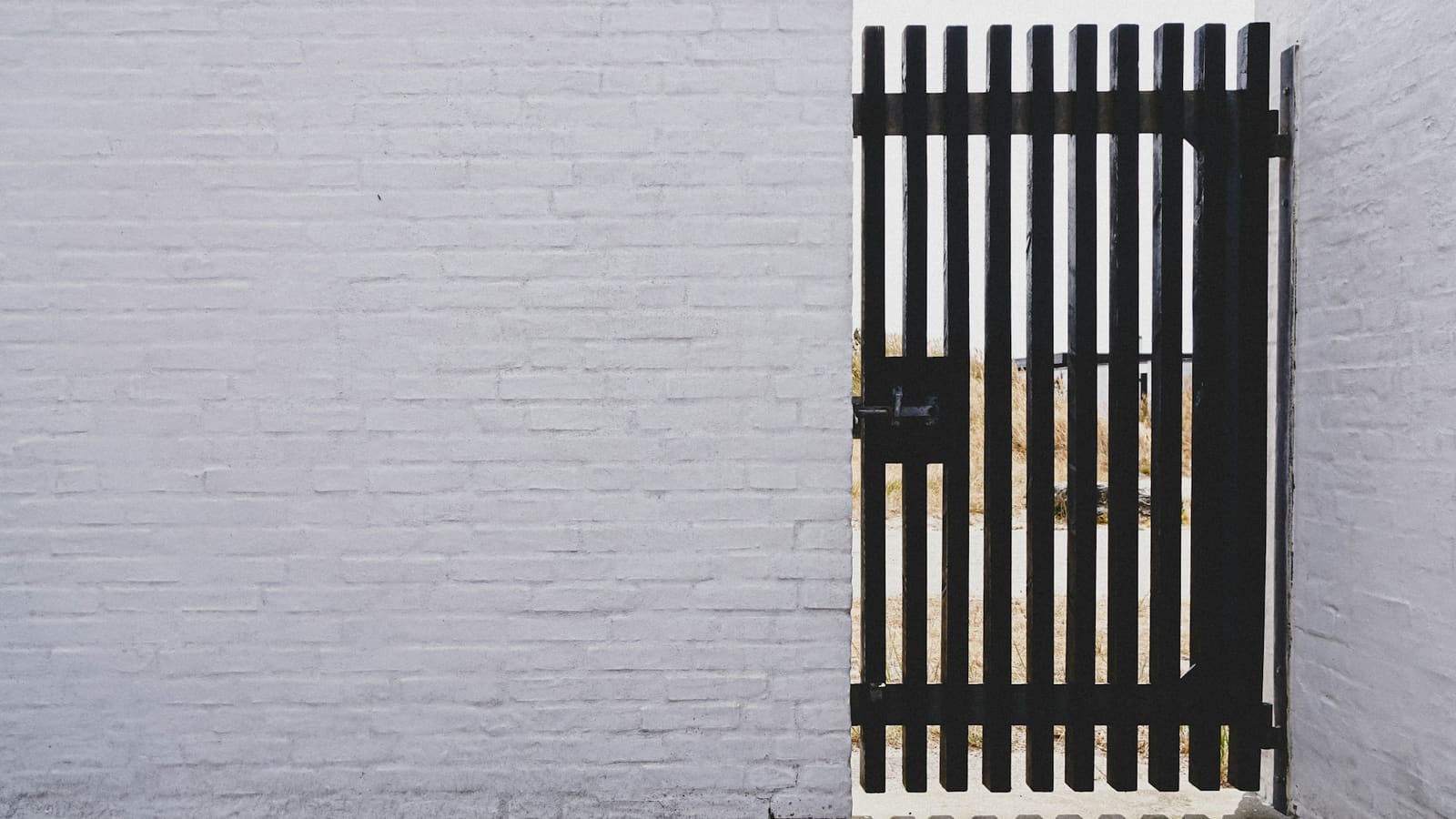 Black wooden slatted gate set in a white painted brick wall