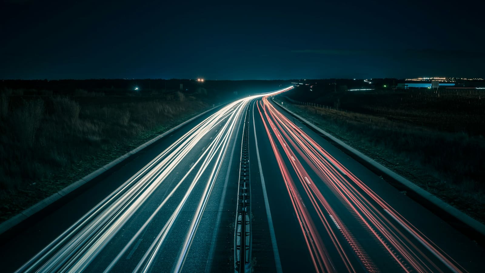 Long exposure light trails streaking along a dark highway beneath a night sky