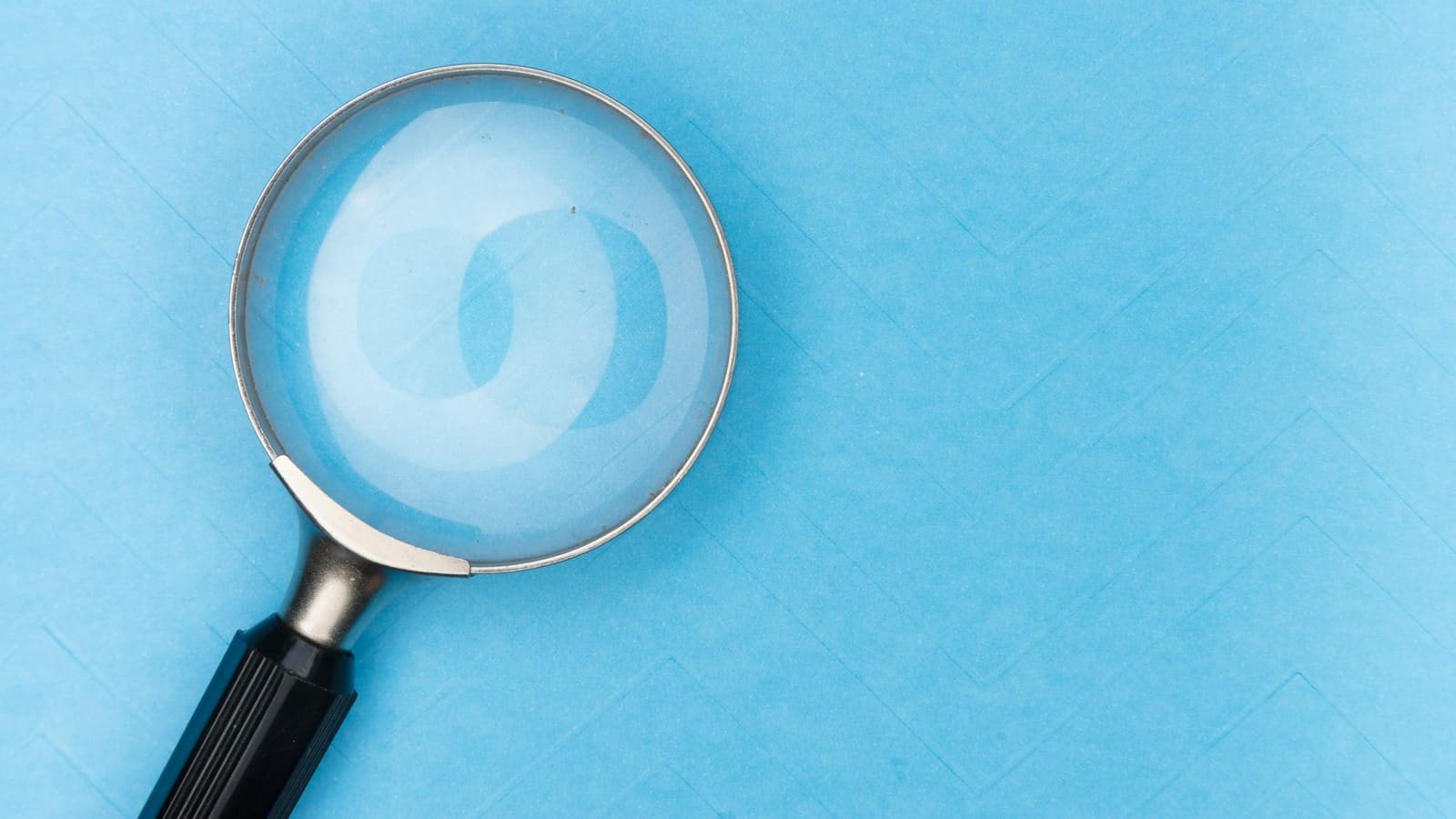 Magnifying glass with a black handle resting on a light blue paper surface