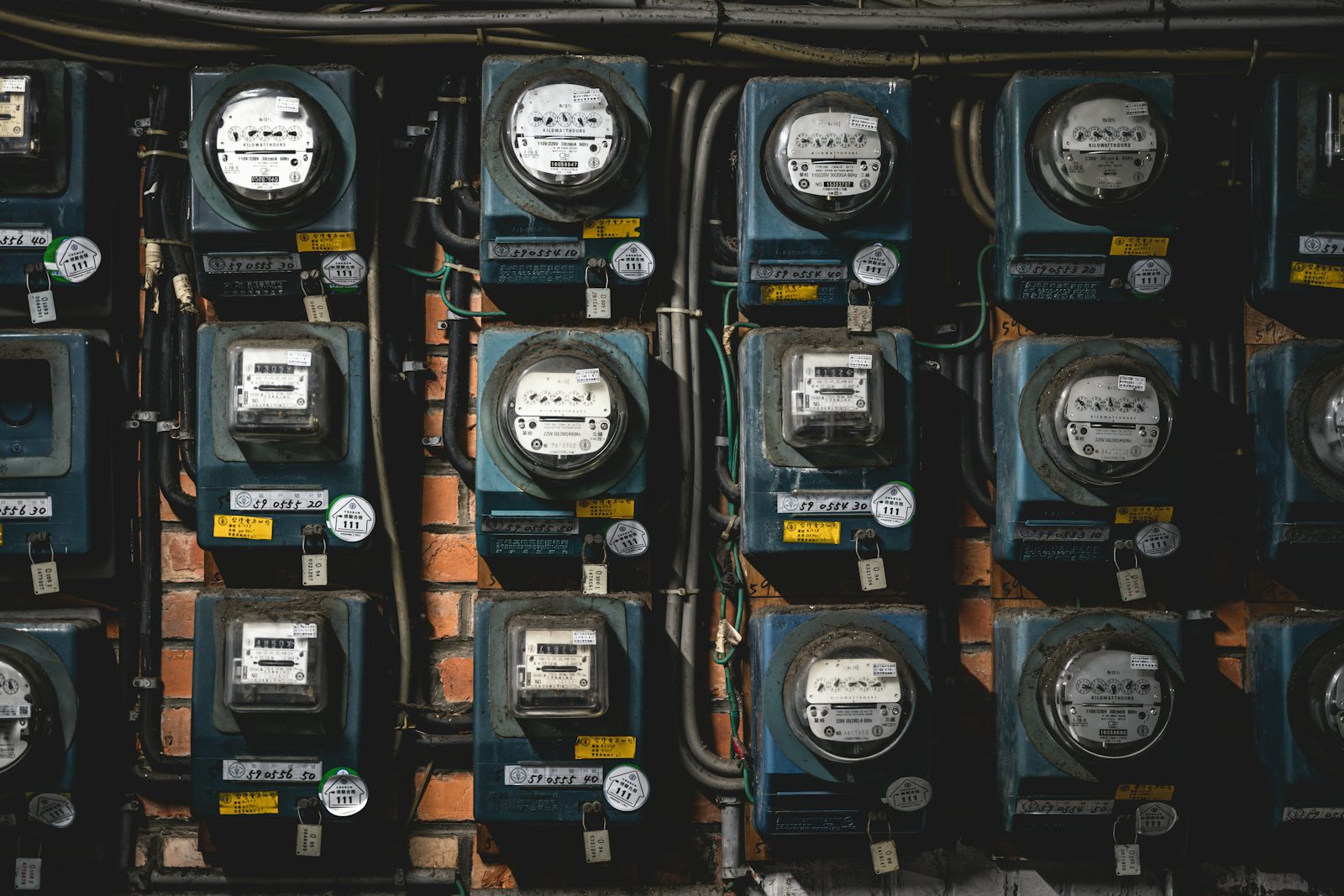 A brick wall covered with rows of blue analog electricity meters, each with its own numbered label and tag