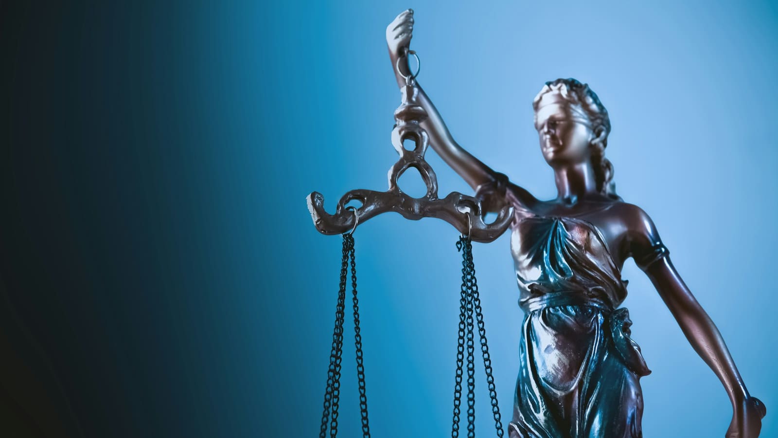 Bronze statue of Lady Justice holding balance scales against a deep blue gradient