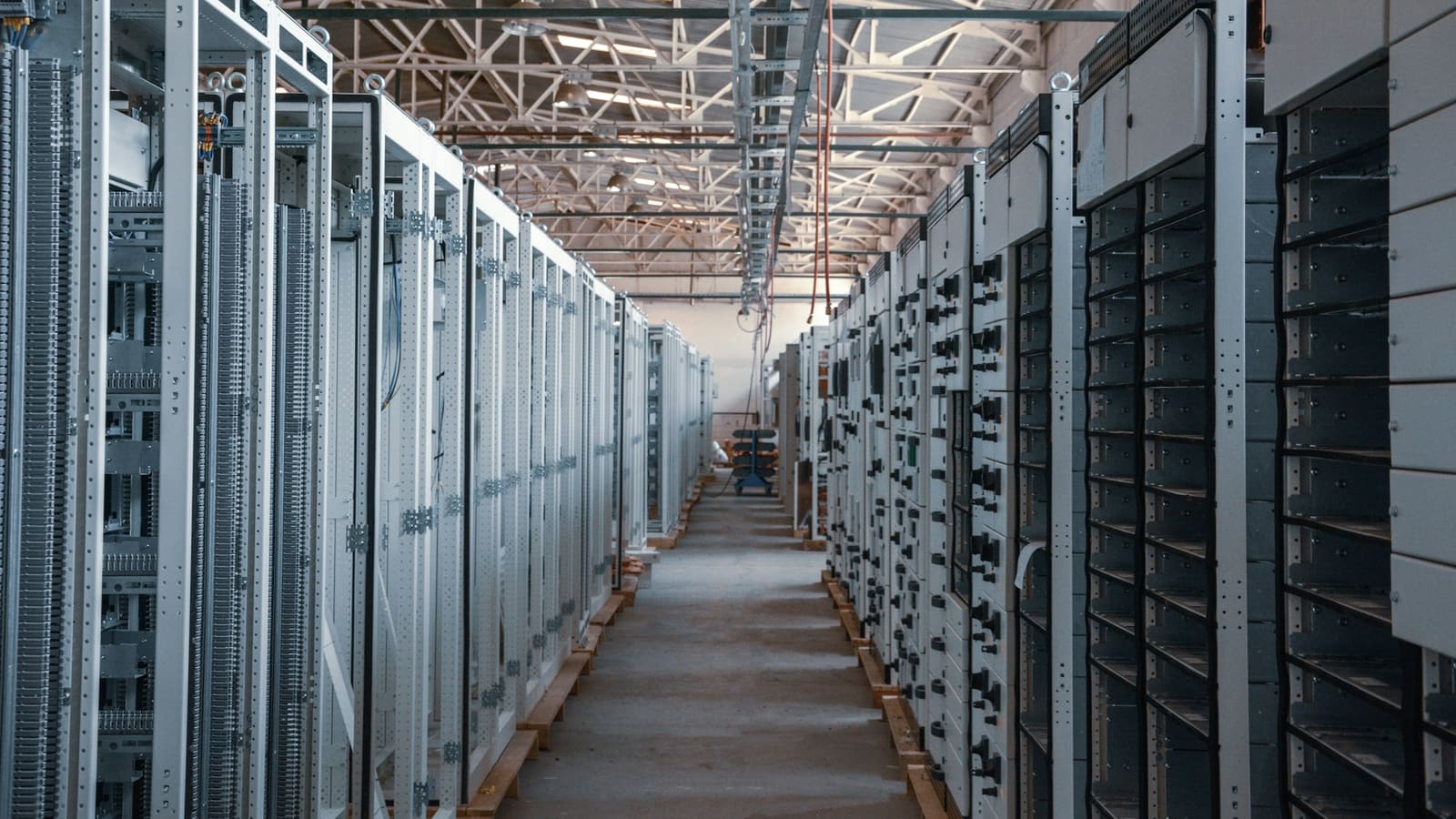 Long aisle between tall grey equipment cabinets under a steel roof structure